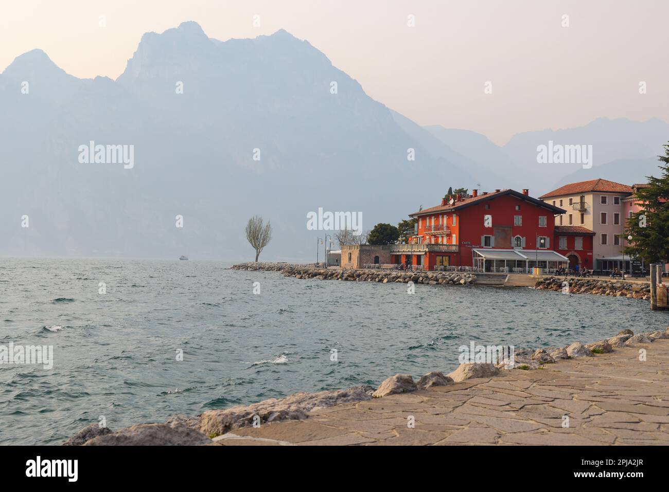 Spring landscape with stone pathway and colorful buildings and mountaind in mist, Lake Garda, Torbole town, Italy, Europe 03 20 2023 Stock Photo