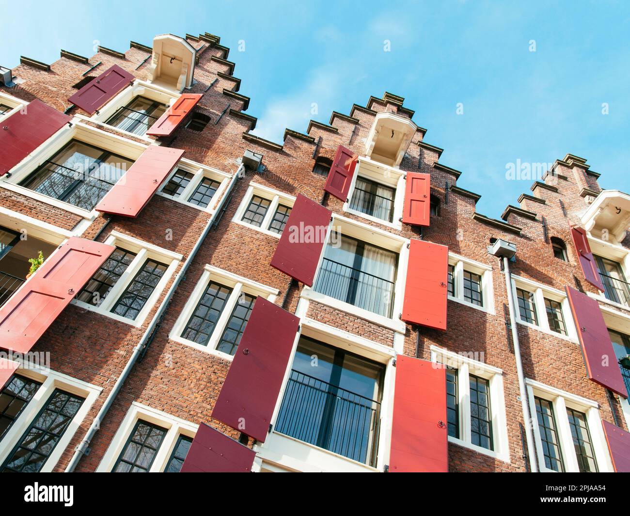 Facedes of canal houses in Amsterdam with red wooden shutters. Stock Photo