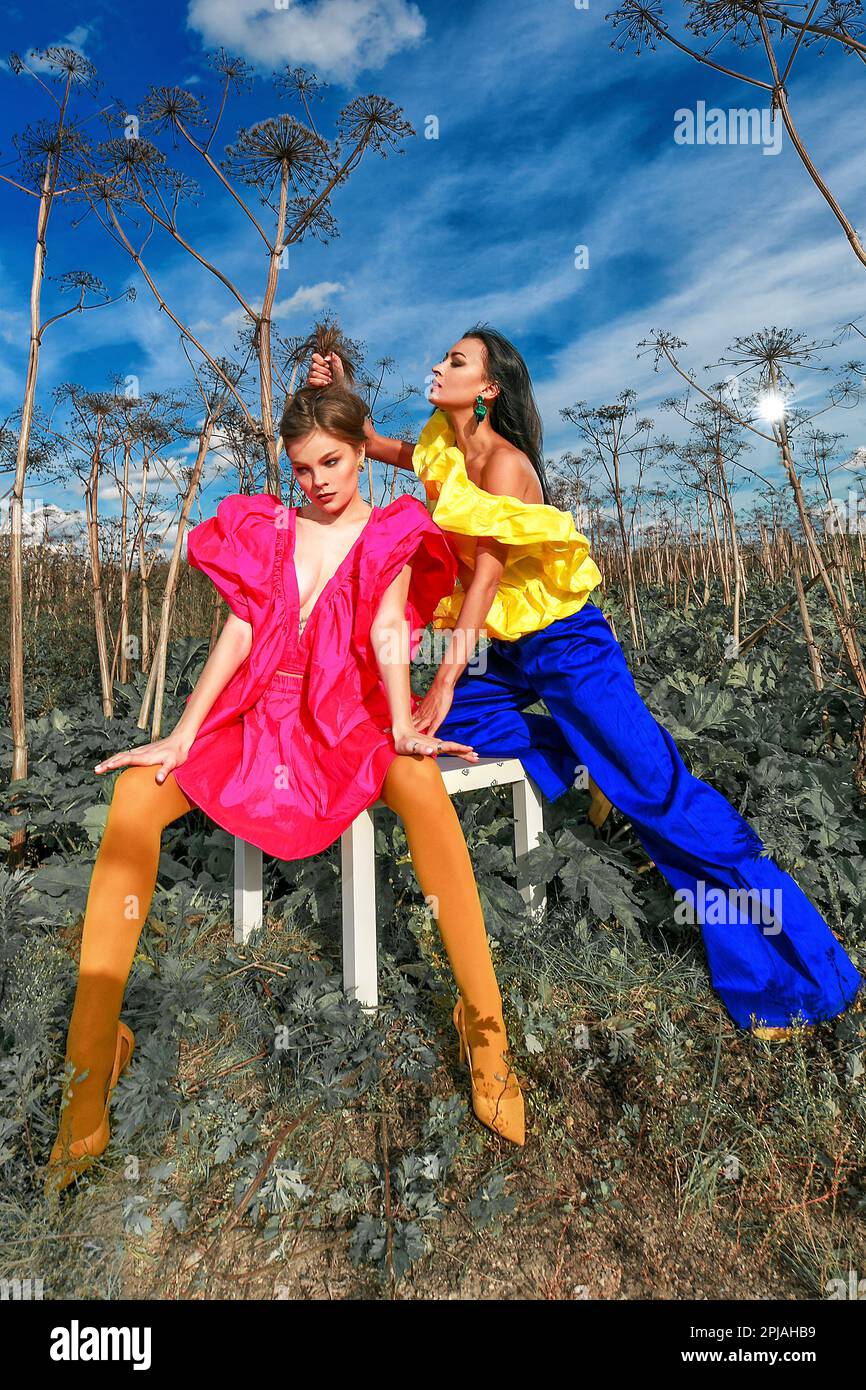 Opposing Models Two models in bright outfits pose against the background of nature ...