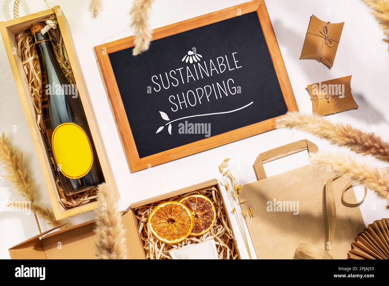 Eco friendly shopping. Craft cardboard gift boxes, wooden box with bottle of champagne and blackboard with text Sustainable Shopping on beige backgrou Stock Photo