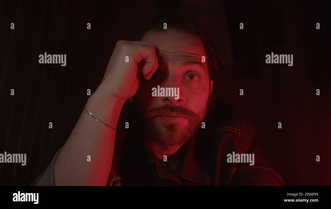 Young, Long-Haired, Bearded Male Model in a Denim Jacket Striking a Pose and Looking into the Camera under a Red LightClose-Up Shot of a Young, Long-H Stock Photo