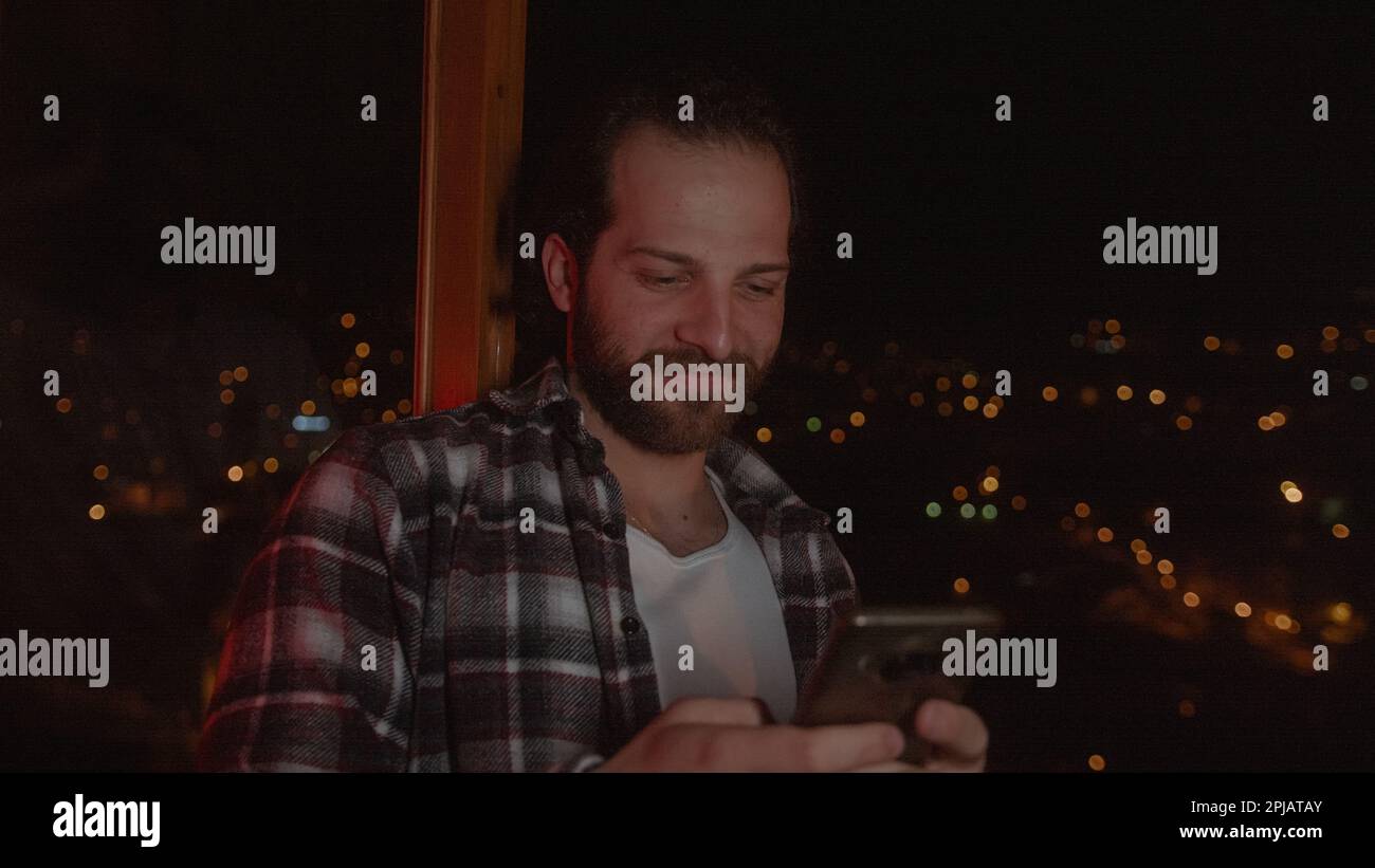 Beard in Checked Shirt Uses Messaging or Apps on Smartphone in a Stunning Home with a View Stock Photo