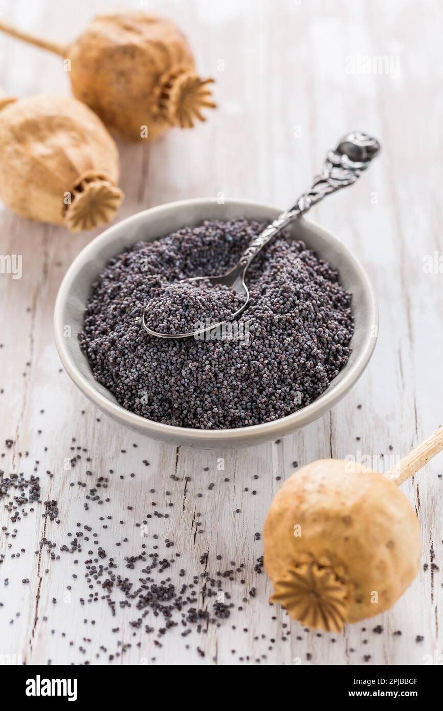 Organic poppy seeds in small bowl with poppy heads on wooden background ...