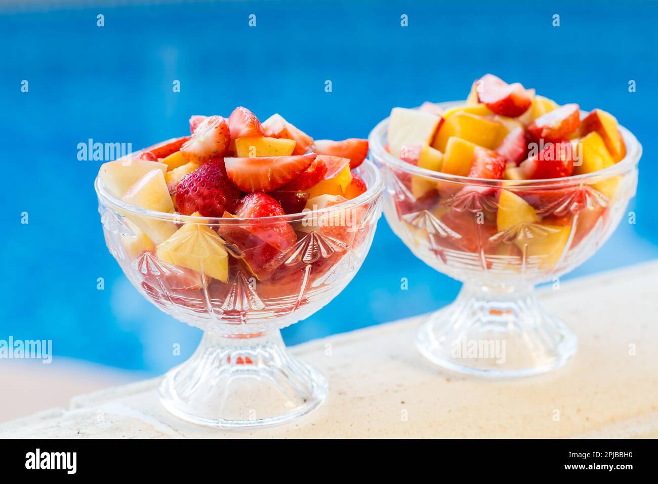 Two bowls of fresh fruit salad with swimming pool in background. Concept of healthy eating, antioxidants and summer time Stock Photo