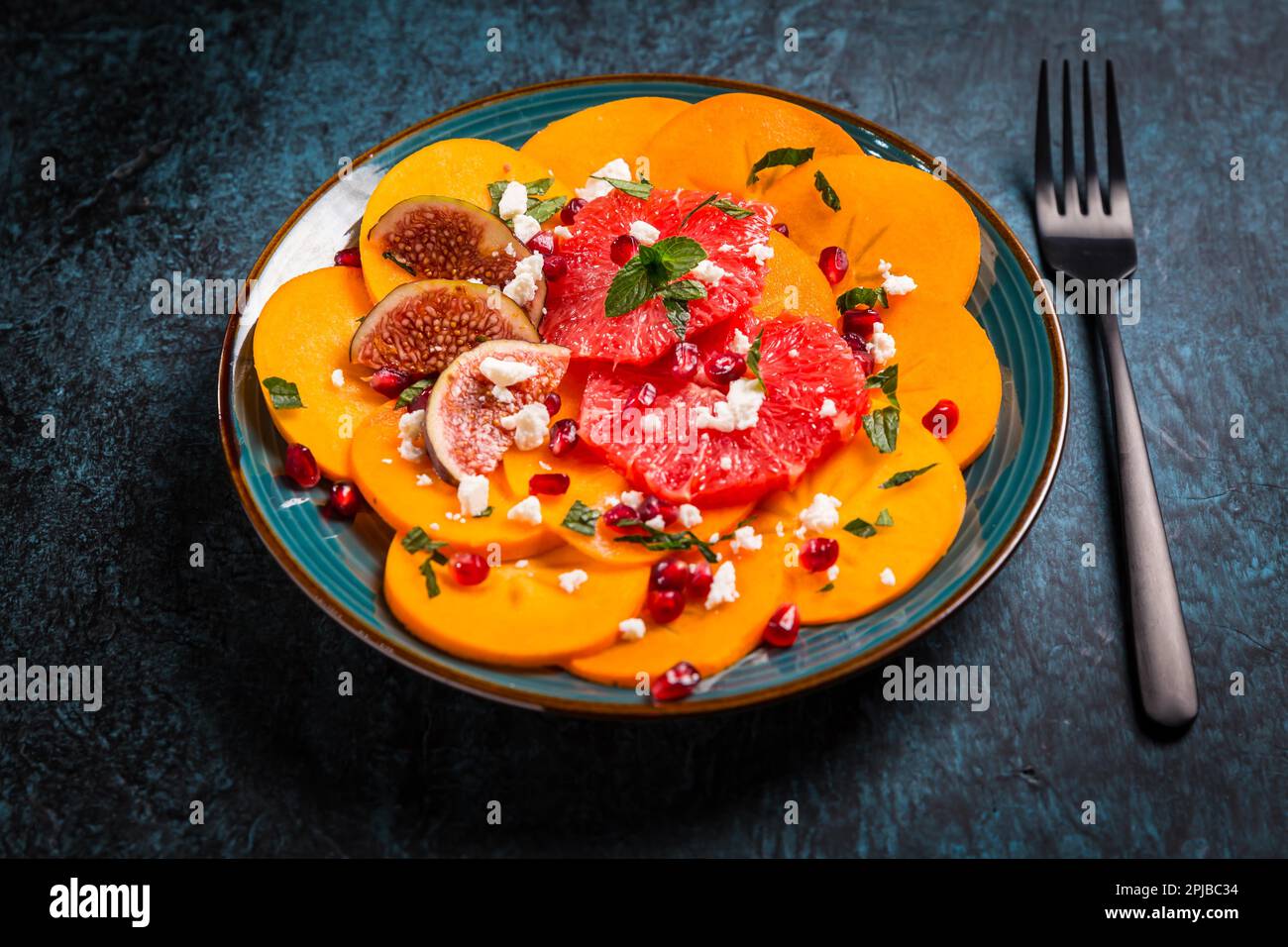 Healthy winter salad - Persimmon carpaccio salad with pomegranate, feta cheese, pink grapefruit and figs Stock Photo