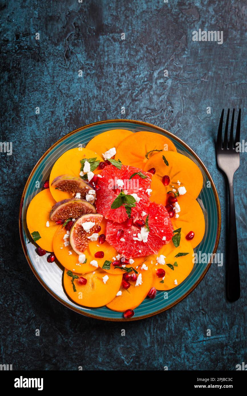Healthy winter salad - Persimmon carpaccio salad with pomegranate, feta cheese, pink grapefruit and figs Stock Photo