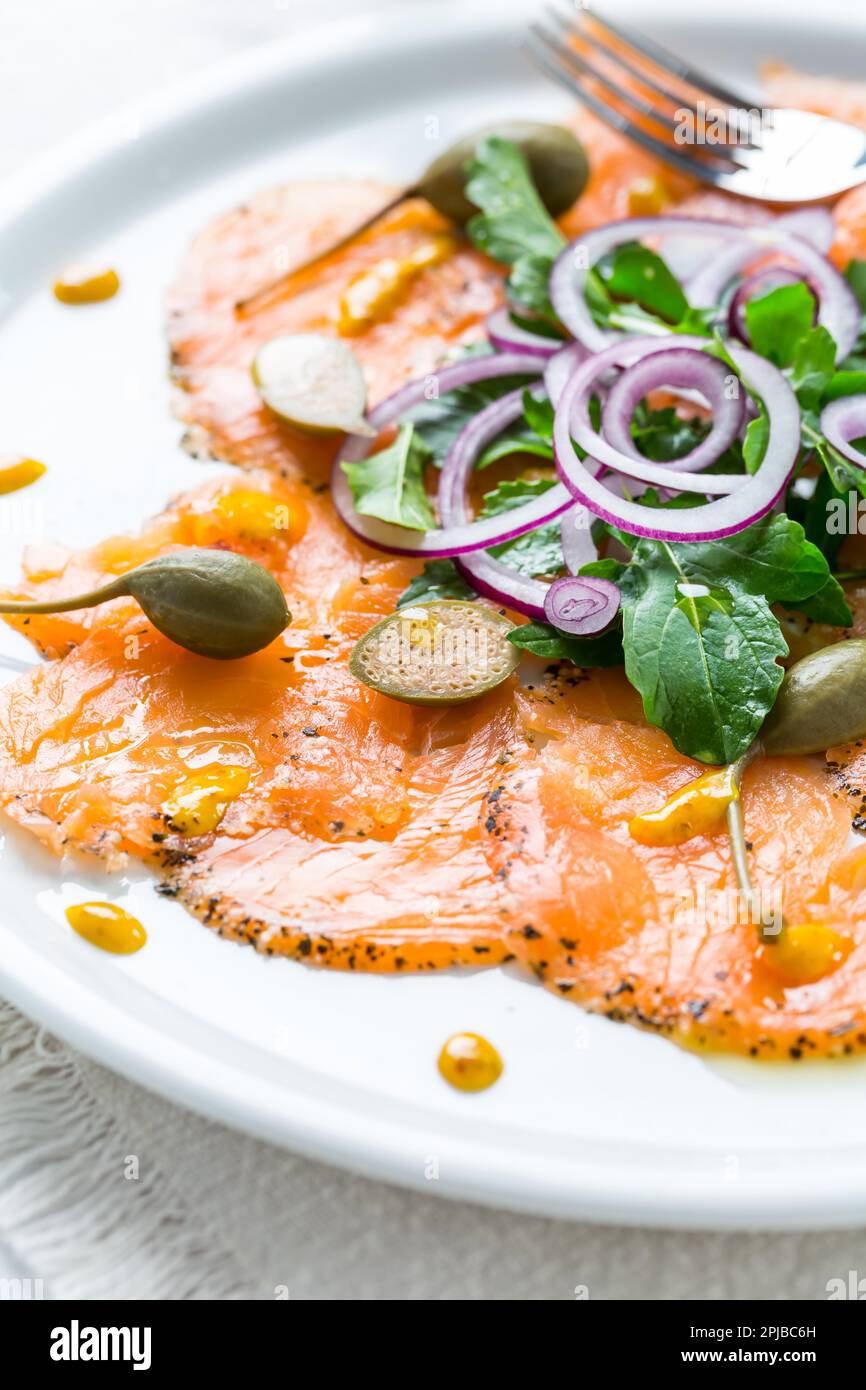 Salmon carpaccio and arugula salad with onions and capers on white plate Stock Photo