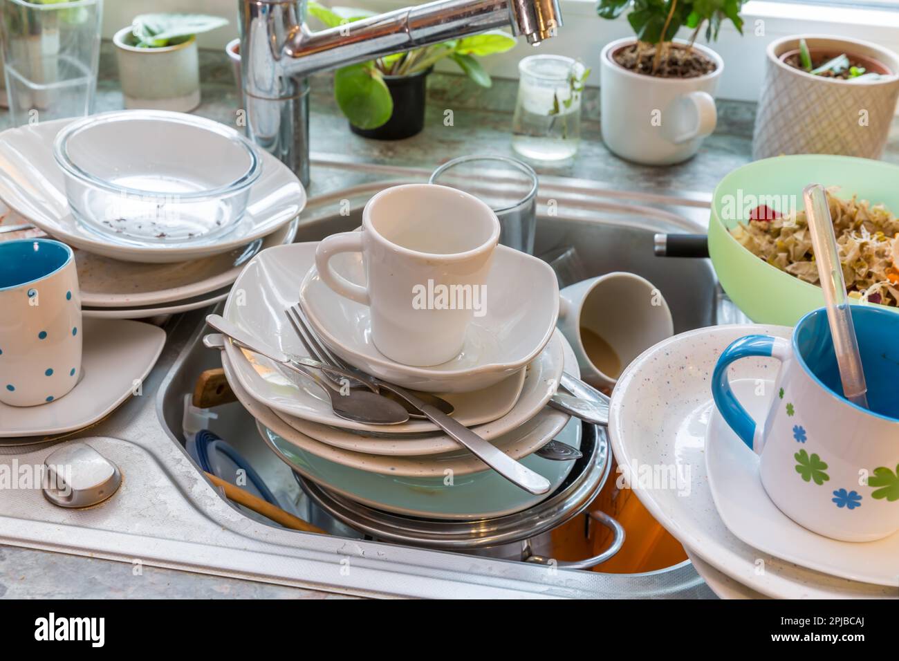 Messy kitchen counter with pile of dirty dishes in sink - Compulsive Hoarding Syndrome Stock Photo