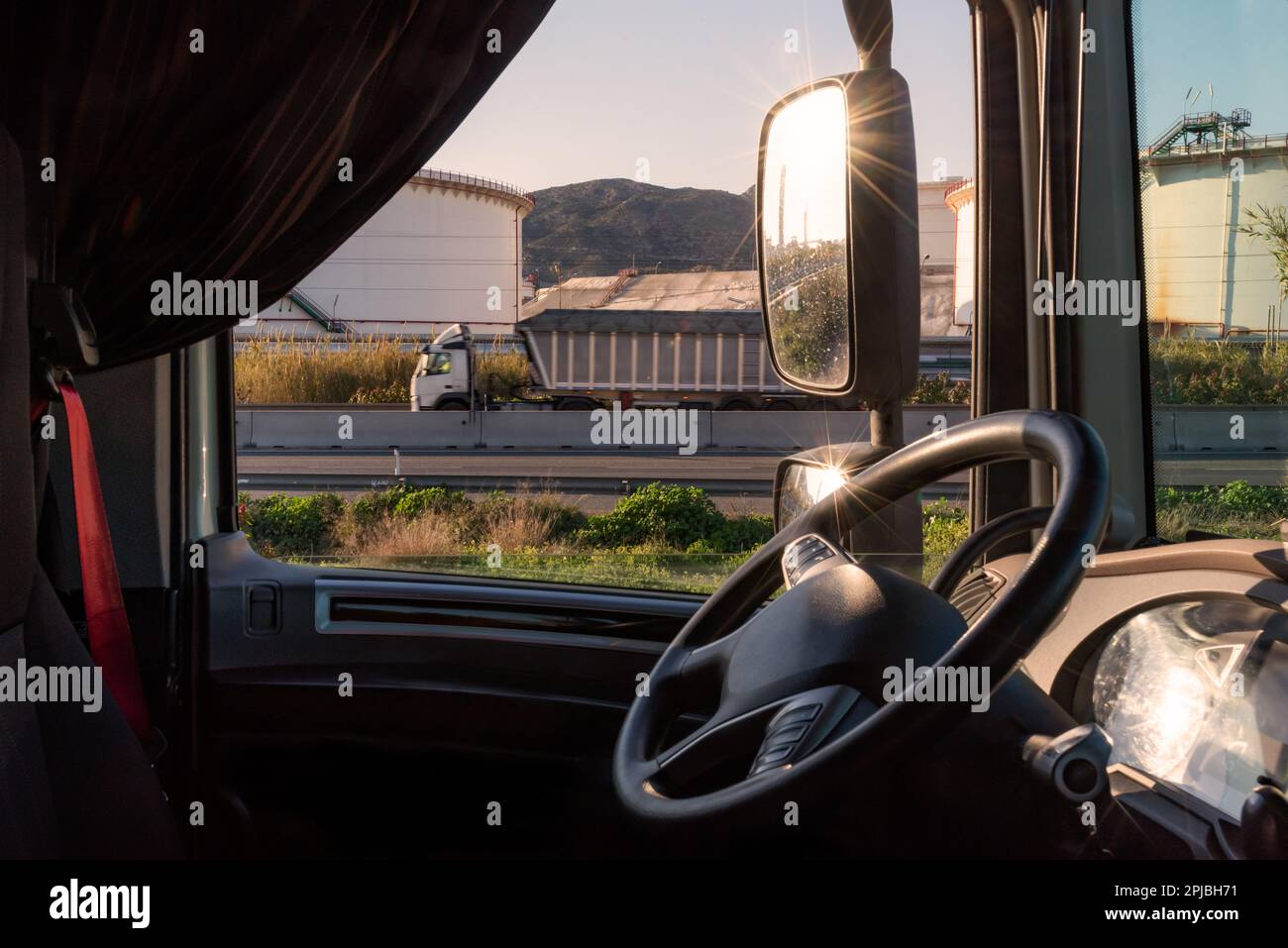 View of the conduction post of a truck with the steering wheel in the foreground and deposits of an industrial zone. Stock Photo
