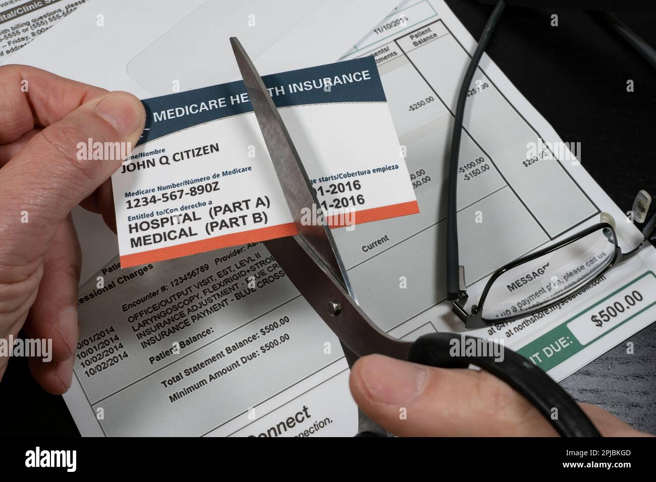 Selective focuse of man cutting a fake Medicare cut with fake hospital bill in background. Concept of high cost of medical care. Stock Photo