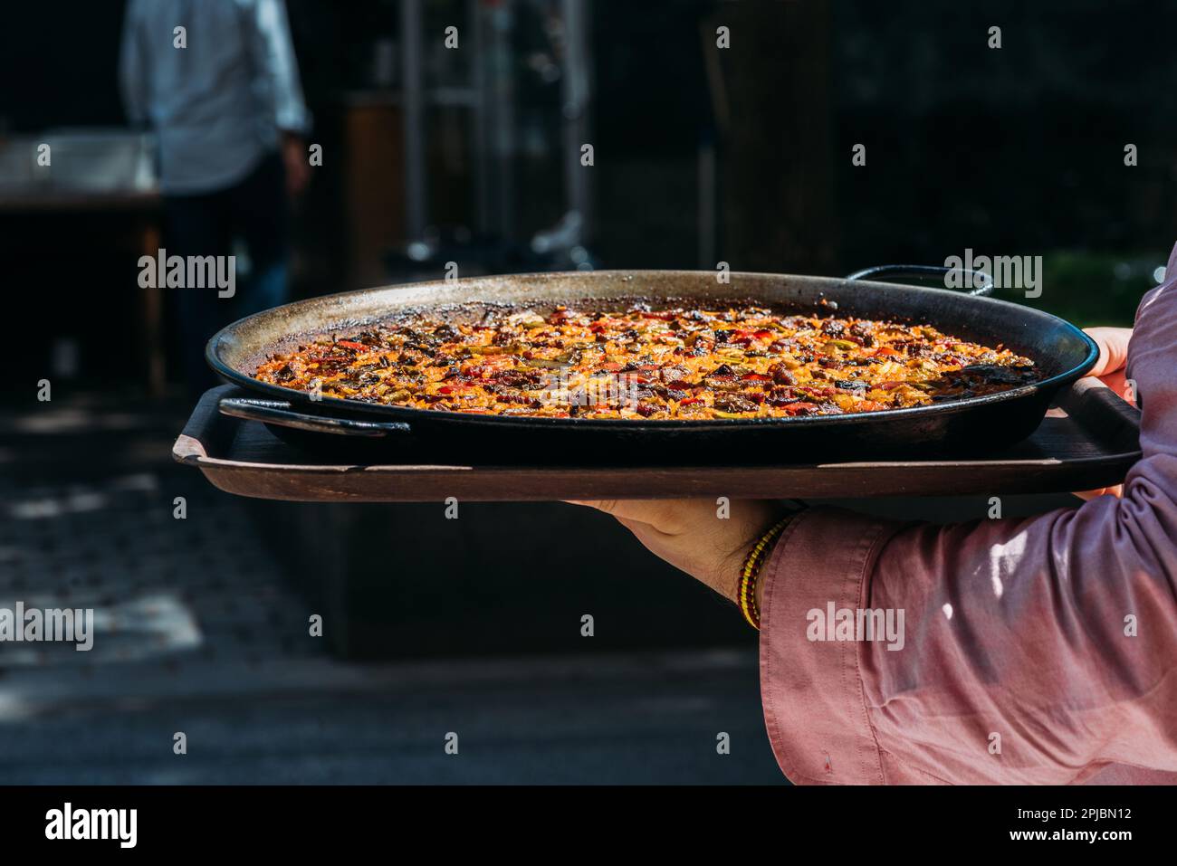 Waiter holding a giant Spanish paella dish outside a restaurant terrace Stock Photo
