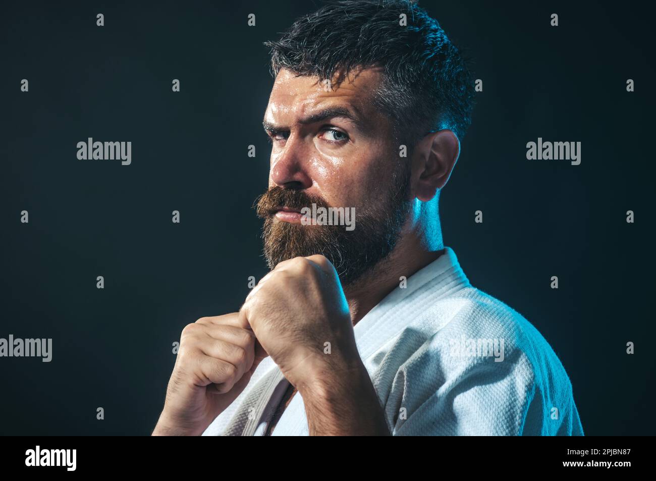 Man training karate at gym. Sport and fitness concept. Martial arts fighter. Bearded man in white kimono for sambo, judo, jujitsu with hands clasped Stock Photo