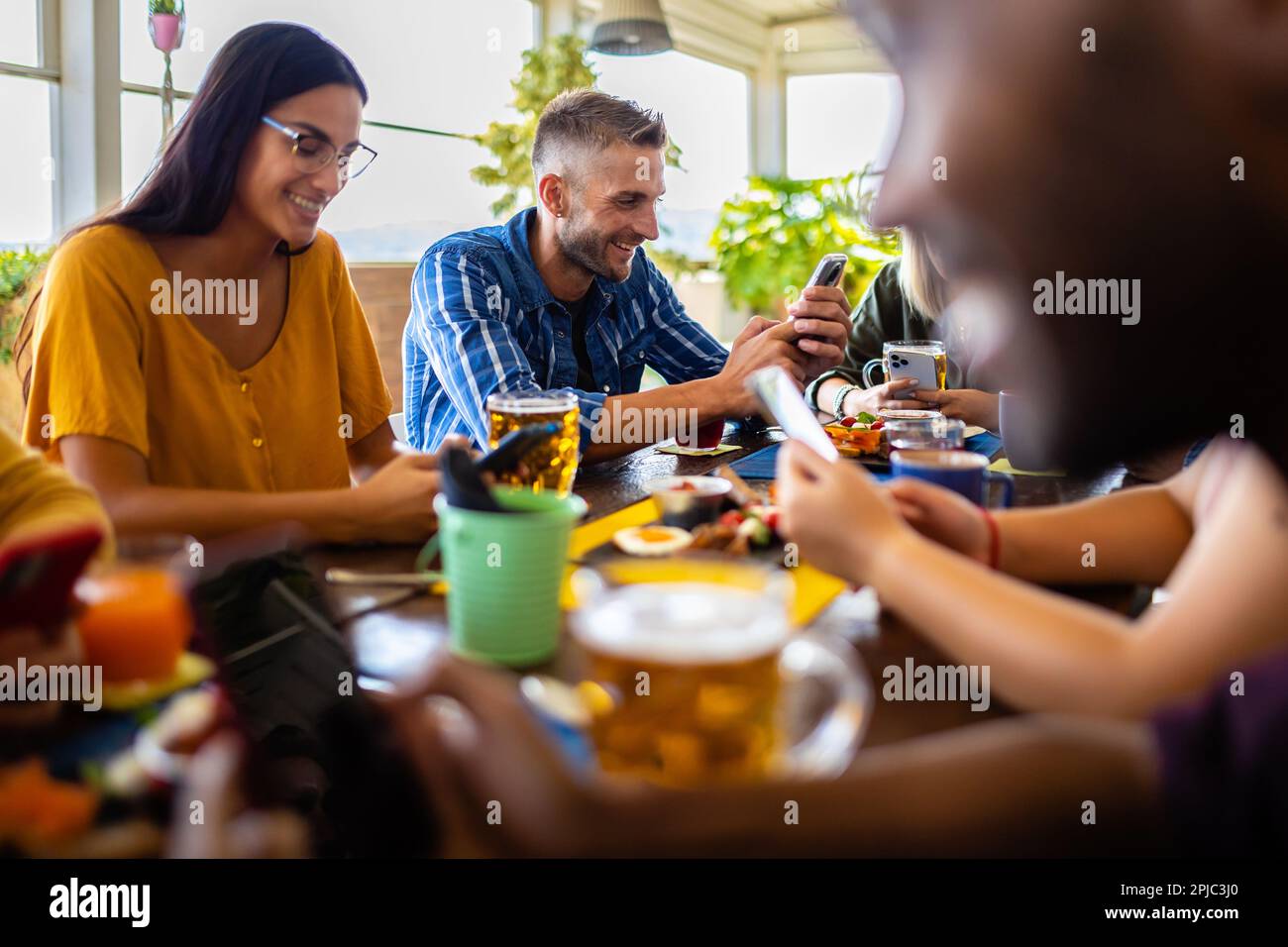 Addicted young people using mobile phone devices sitting at restaurant table Stock Photo