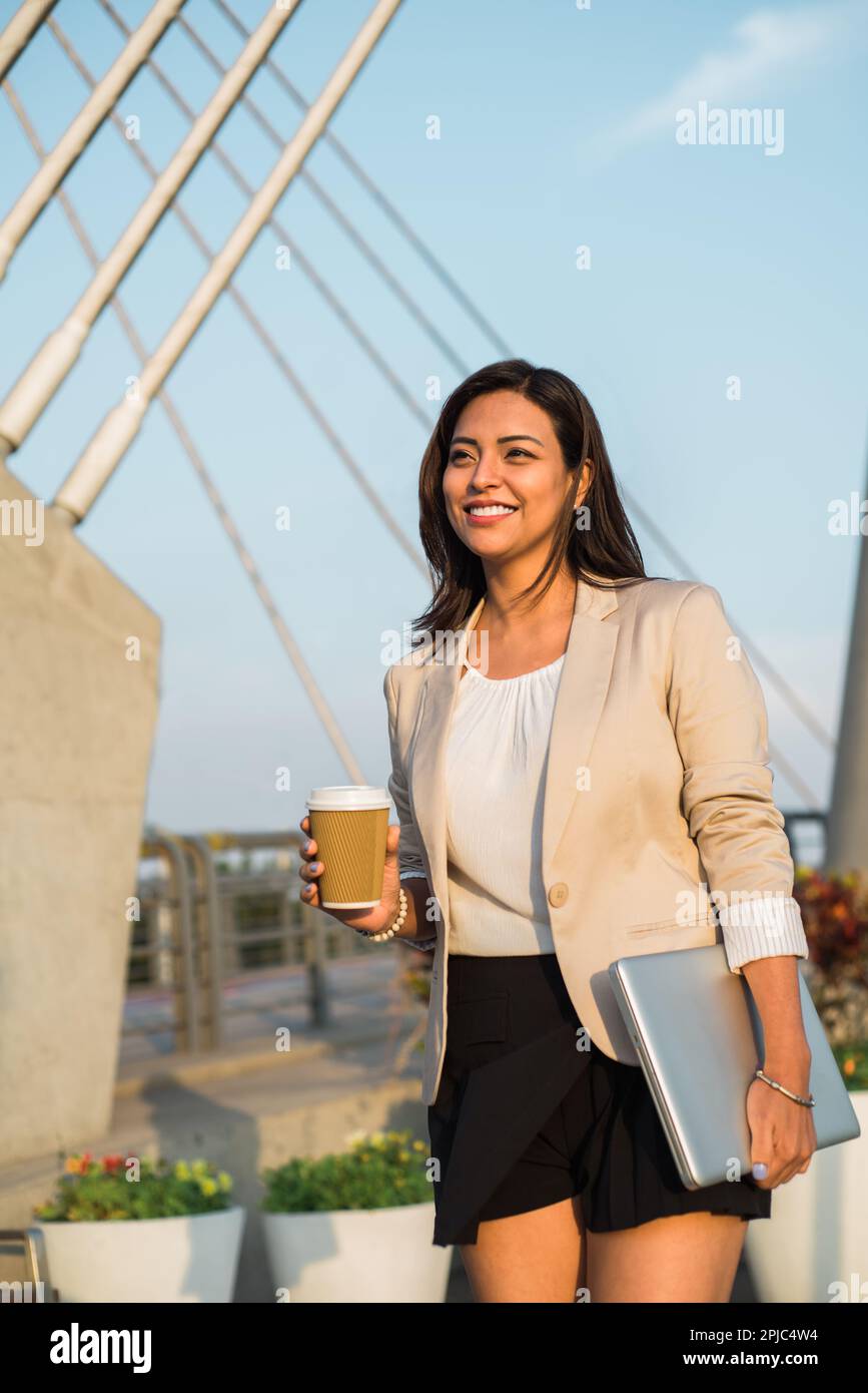 Latina executive walking to work with a coffee and her personal computer. Stock Photo