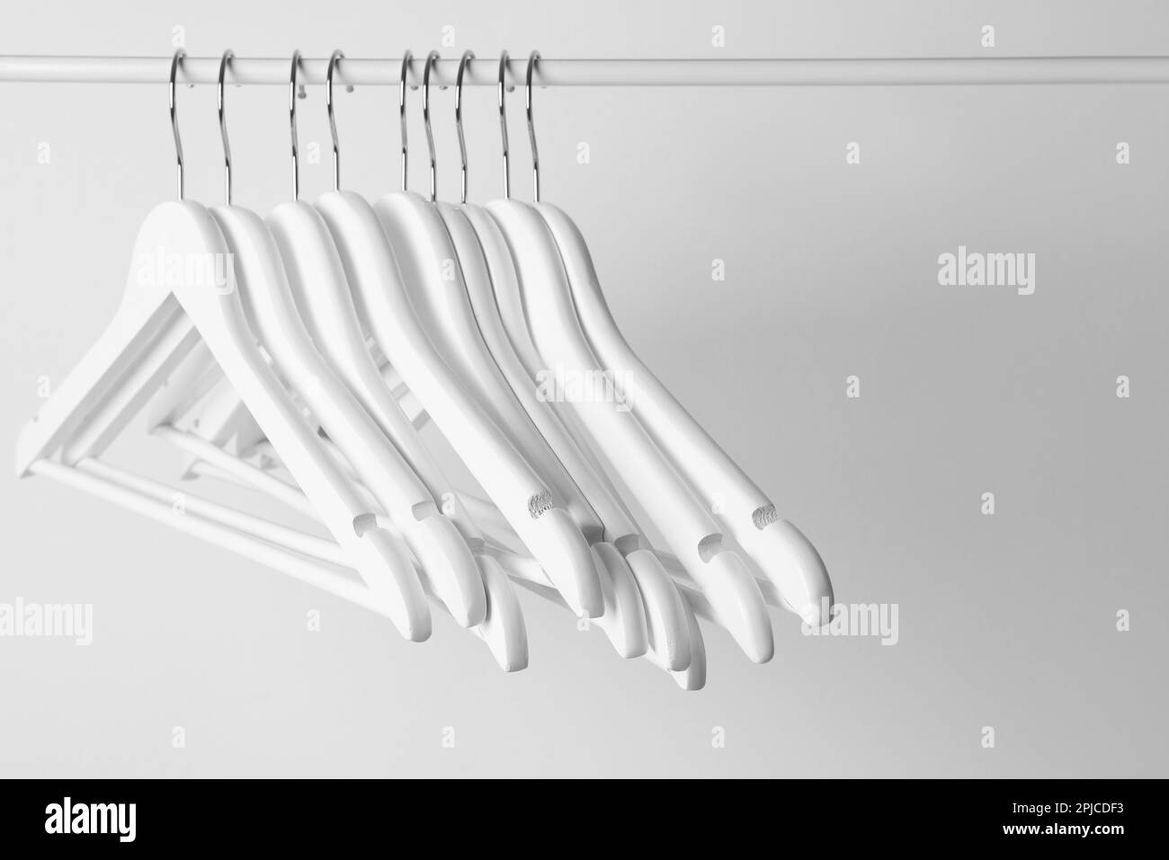 White clothes hangers on metal rail against light background Stock