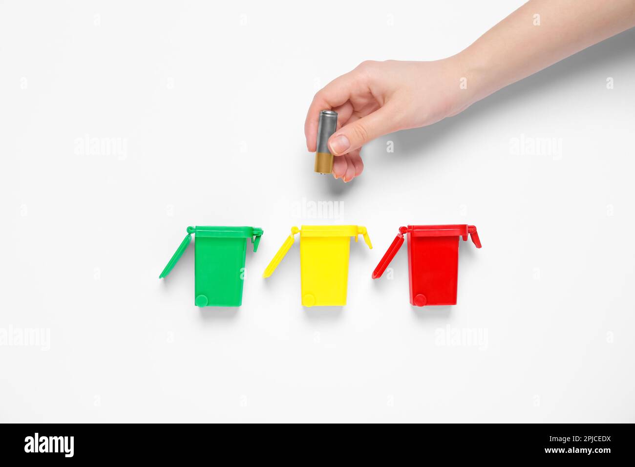 Woman throwing battery into trash bin on white background, top view