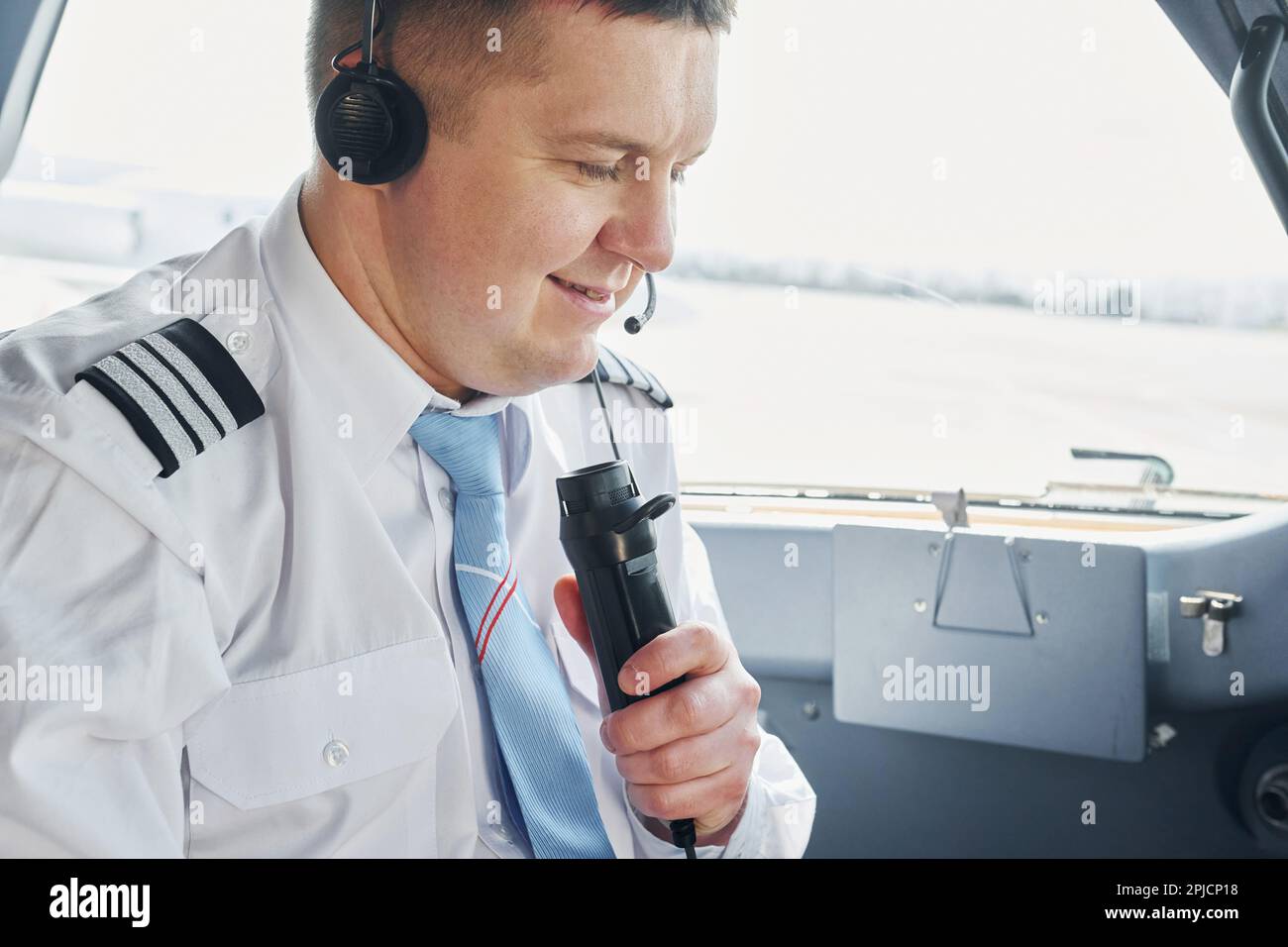 Talks to a mic. Pilot in formal wear sits in the cockpit and controls