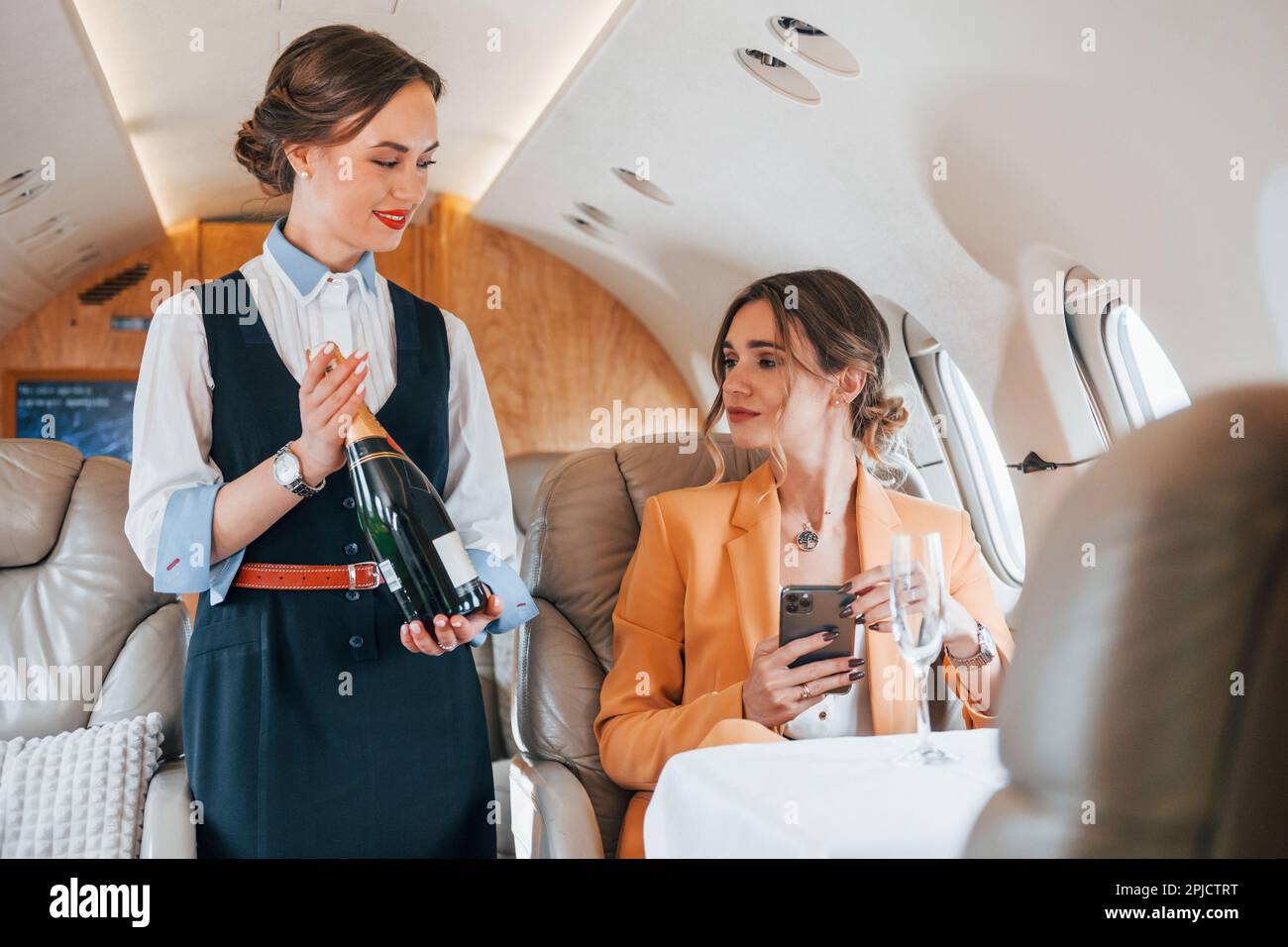 Stewardess with bottle of alcohol. Young passenger woman in yellow