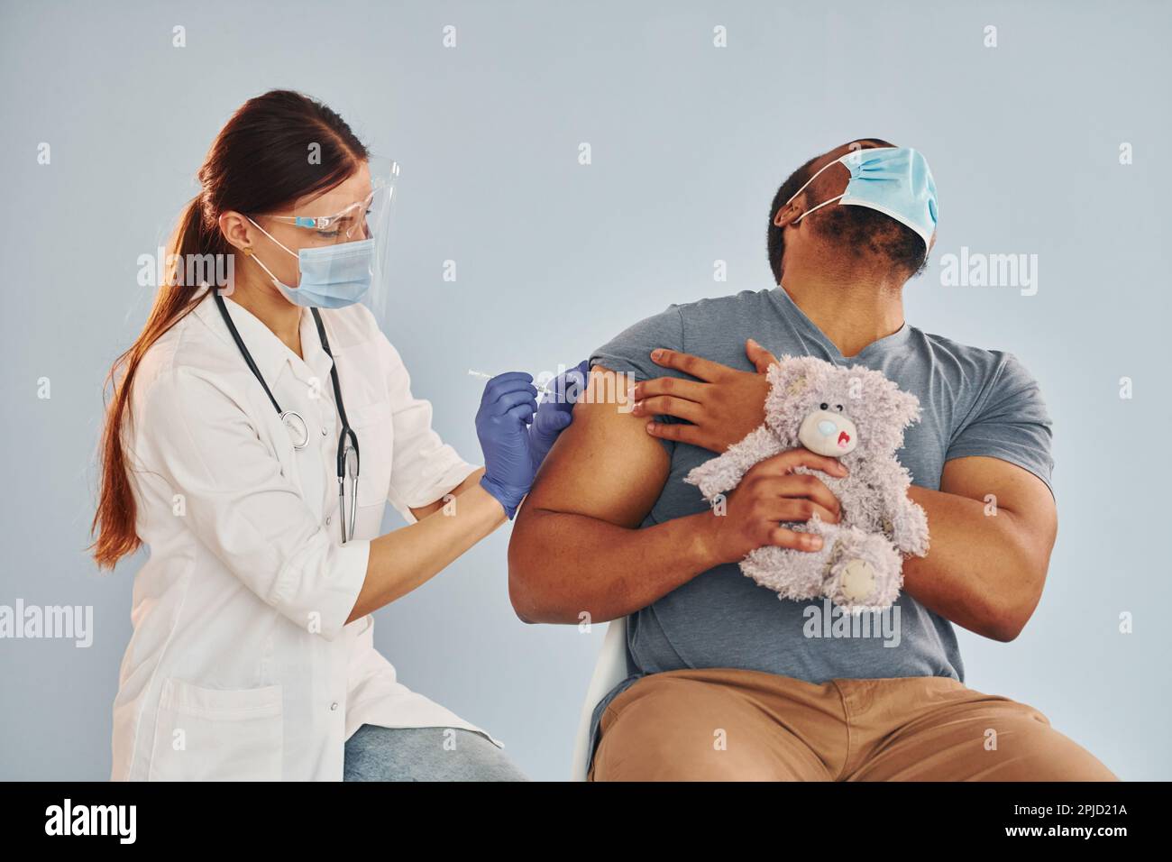 Scared guy with teddy bear. Female doctor giving injection to african ...