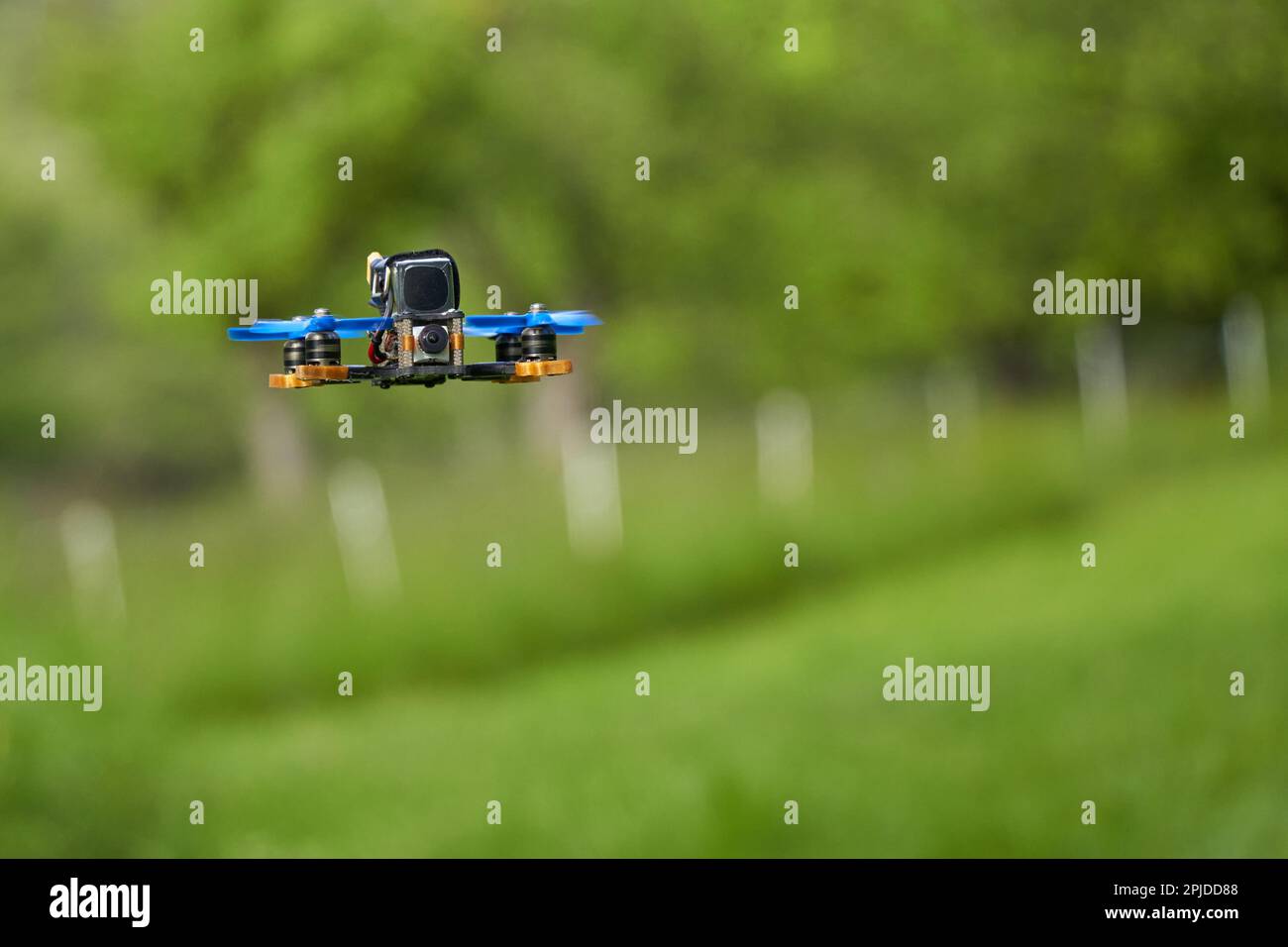 Small race copter also drone with blue propellers and black battery over a green meadow in front of a pasture fence. Depth of field. Stock Photo