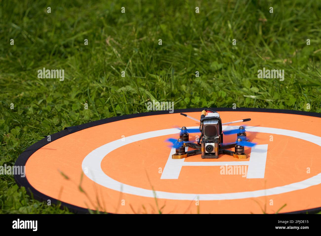 Small quadcopter with blue propellers on an orange landing pad (Landeplatz), which is located in the green meadow. Stock Photo