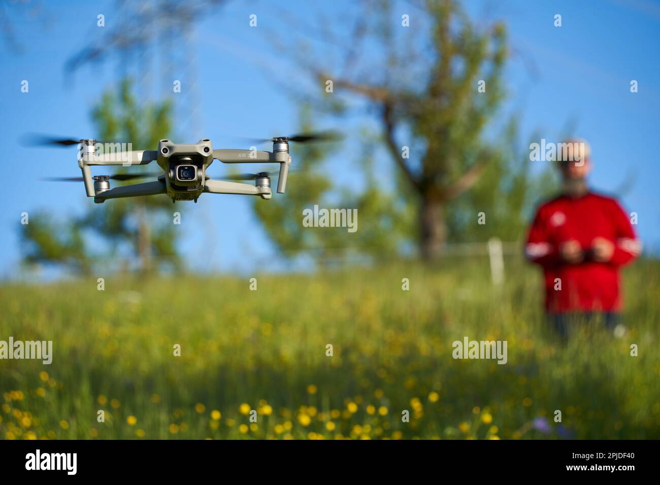 Nürtingen, Germany - May 29, 2021: Drone dji air 2s. Modern multicopter over wildflower field. Pilot with red sweater blurred in background. Stock Photo