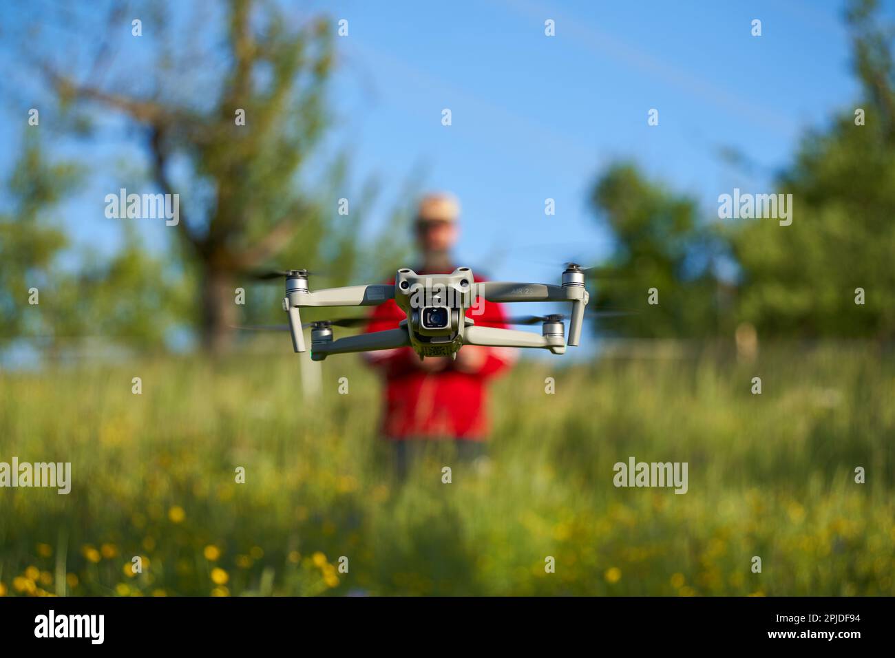 Nürtingen, Germany - May 29, 2021: Drone dji air 2s hovers over a field of wildflowers. Blurred pilot with red jacket controls the unmanned aircraft s Stock Photo
