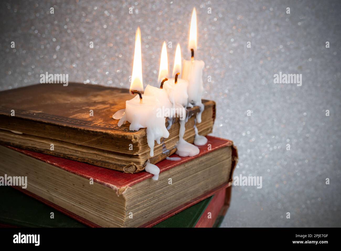 4 burning candles with dripping wax on vintage hard cover books, soft focus close up Stock Photo