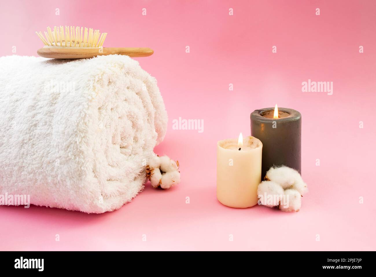 https://c8.alamy.com/comp/2PJE7JP/rolled-white-towel-wooden-hair-brush-cotton-flowers-and-lit-candles-on-pink-backgroud-2PJE7JP.jpg