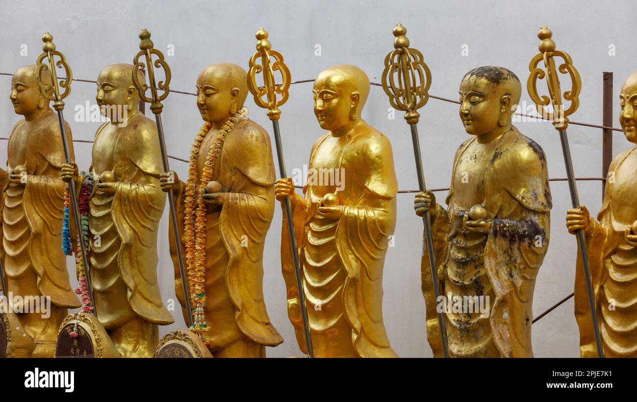 Gold Buddhist statues of golden monks. Kṣitigarbha monk statues holding khakkhara or tiger pewter staffs. Mahayana Buddhism. Cemetery guardians. Stock Photo
