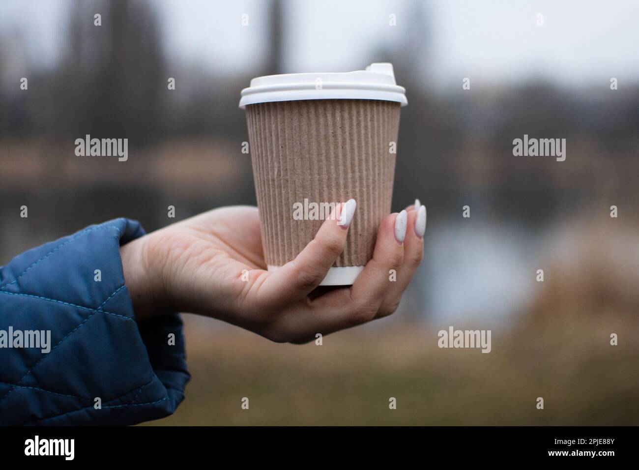 Drink coffee in nature from an ecological paper cup. Warming hands