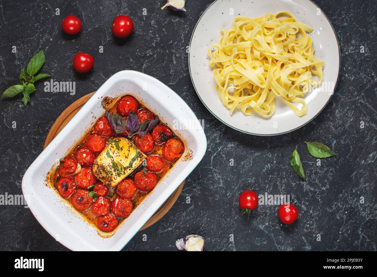 Fetapasta. Trending viral Feta bake pasta recipe made of cherry tomatoes, feta cheese, garlic and herbs in a casserole dish. Top view Stock Photo