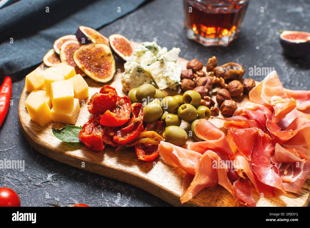 Antipasto platter with ham, prosciutto, blue cheese, dried tomatoes, figs and olives on a wooden bord. Stock Photo