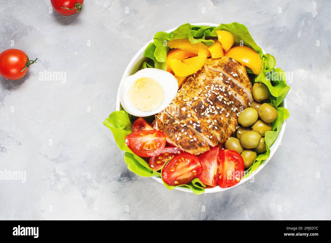 Buddha bowl salad with grilled chicken breast slices, cherry tomatoes, eggs, pepper, olive, lettuce and seeds on concrete background. Healthy food, cl Stock Photo