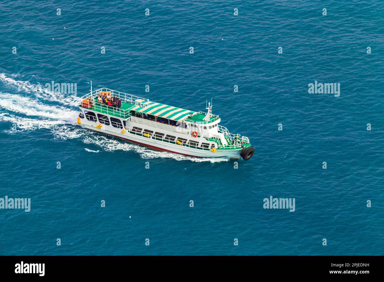 Passenger ferry with green decks sails the Japan Sea on a sunny day, aerial view. Busan, South
