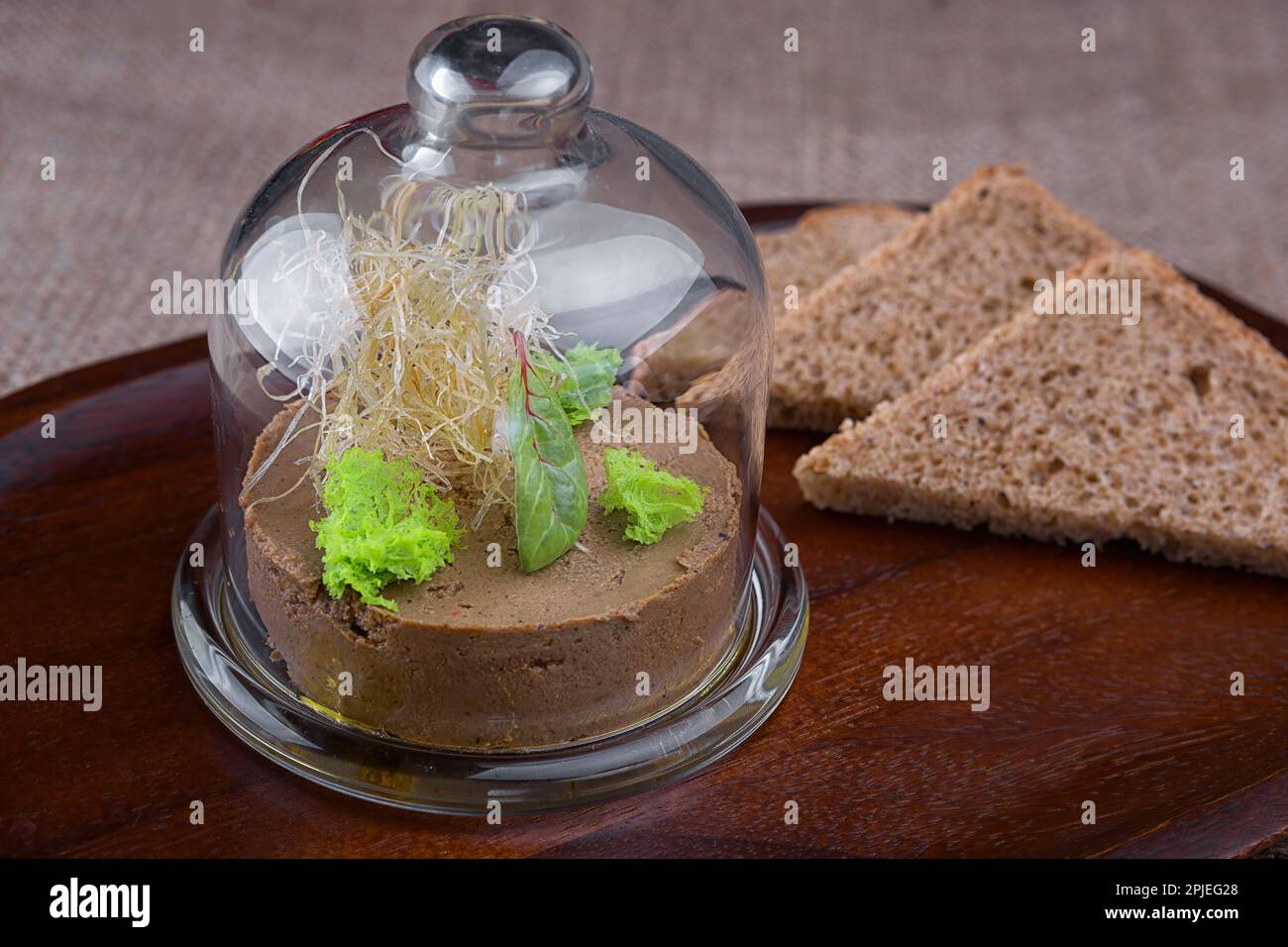 Rich and creamy liver pate with herbs and toasted bread under glass
