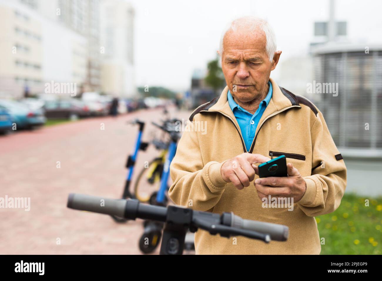 Old man using smartphone to activate e-scooter Stock Photo