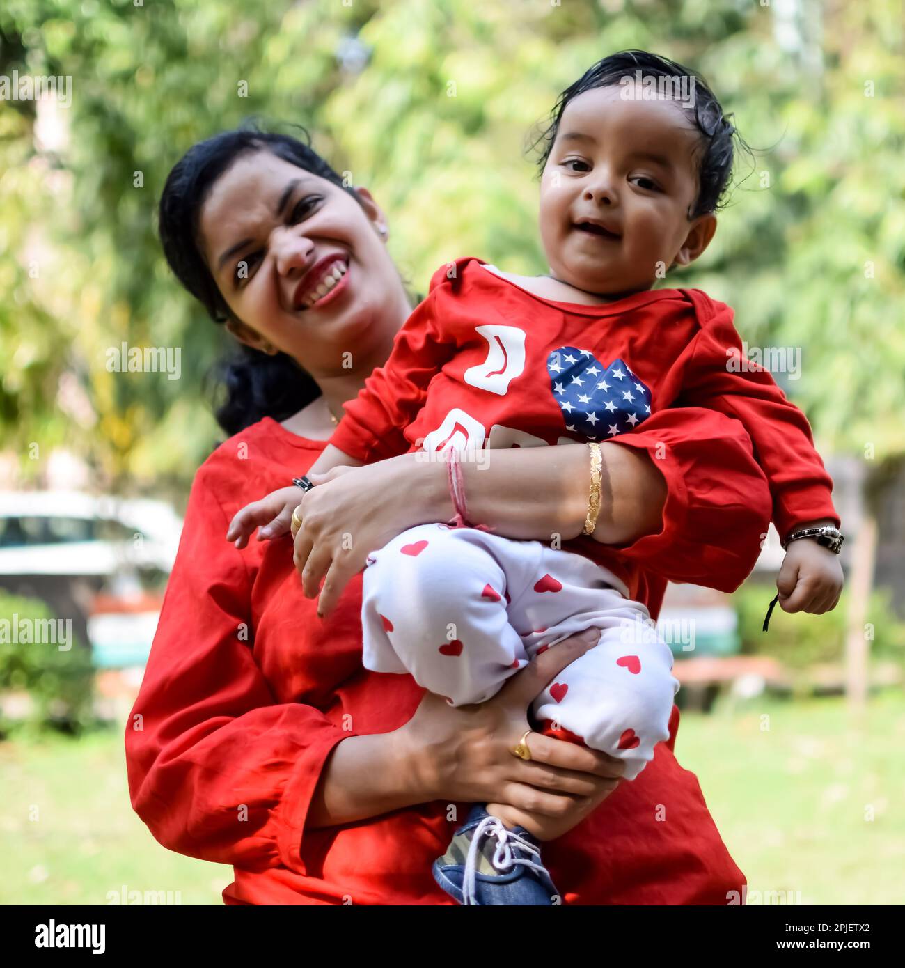 Loving mom carrying of her baby at society park. Bright portrait of happy mum holding child in her hands. Mother hugging her little 9 months old son. Stock Photo