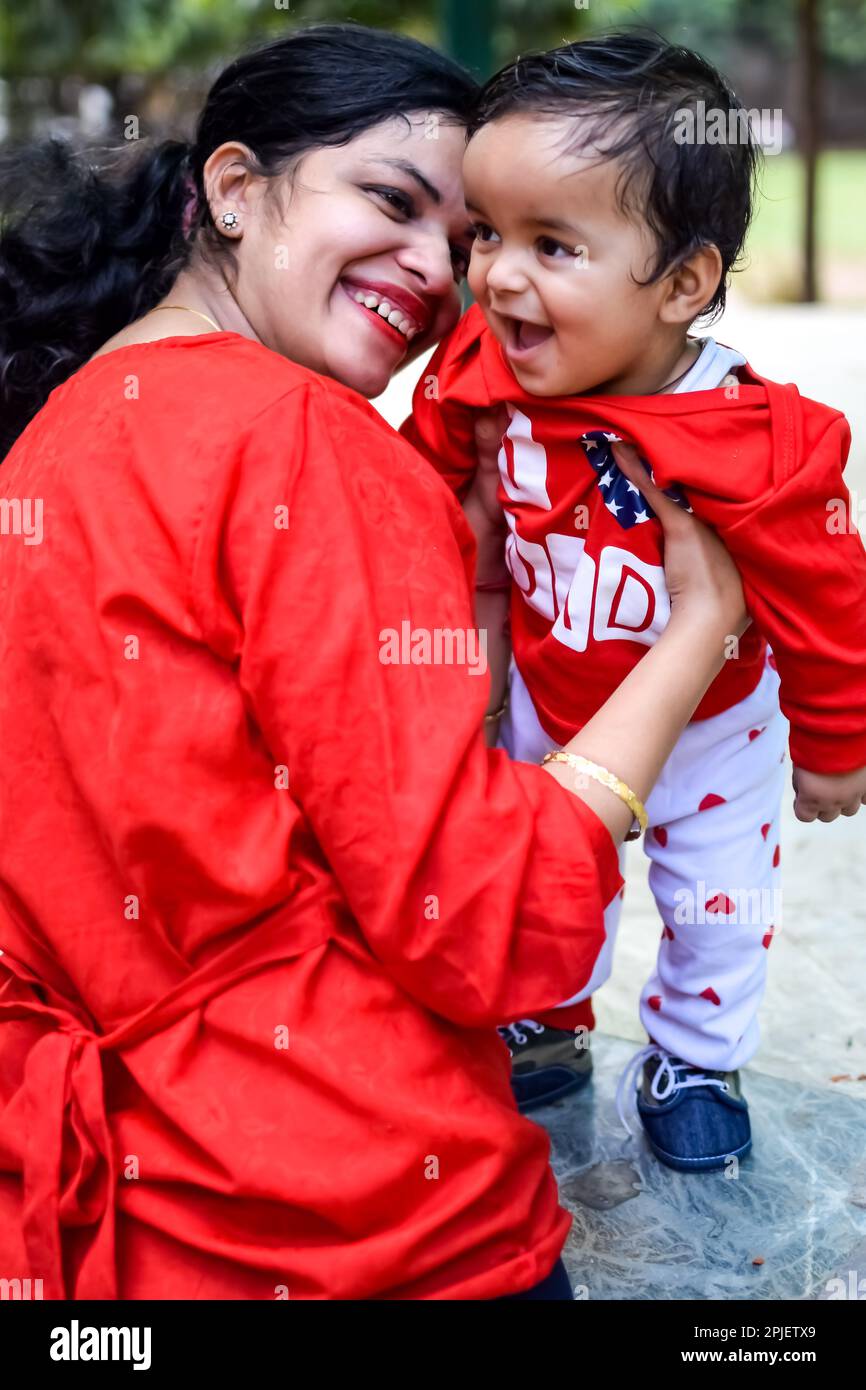 Loving mom carrying of her baby at society park. Bright portrait of happy mum holding child in her hands. Mother hugging her little 9 months old son. Stock Photo