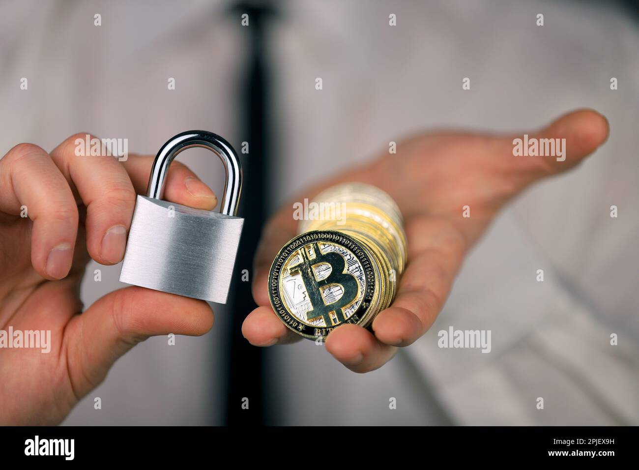 A businessman holds a silver padlock and physical version of bitcoin in his hands. Prohibition of cryptocurrencies, regulations, restrictions or secur Stock Photo