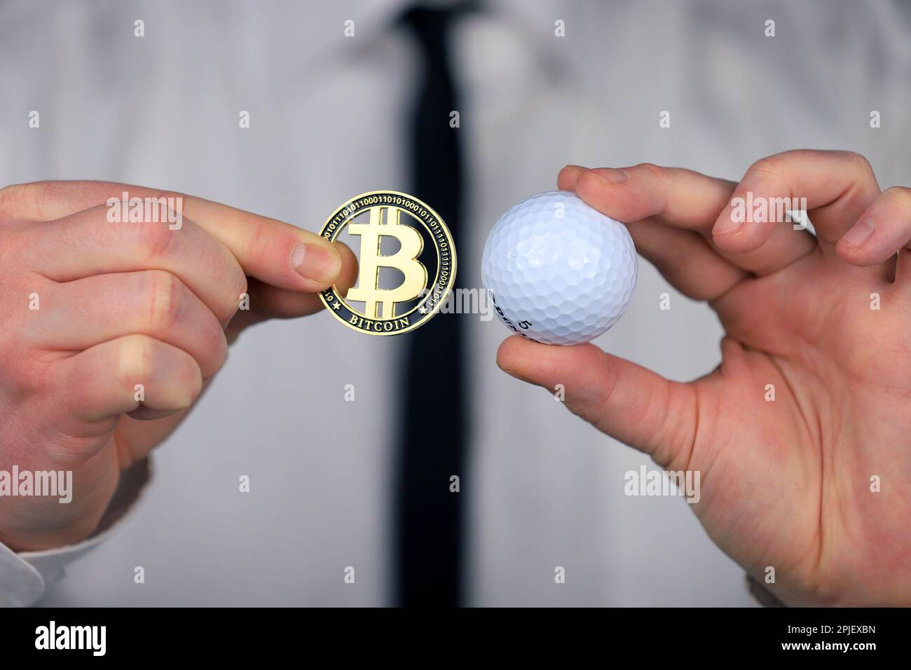 A businessman in a white shirt and black tie holding golf ball and bitcoin  in his hands Stock Photo - Alamy