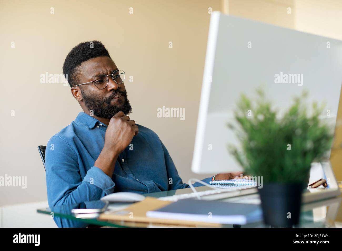 Thoughtful black businessman sitting at workplace and looking at computer screen, thinking about problem solution Stock Photo