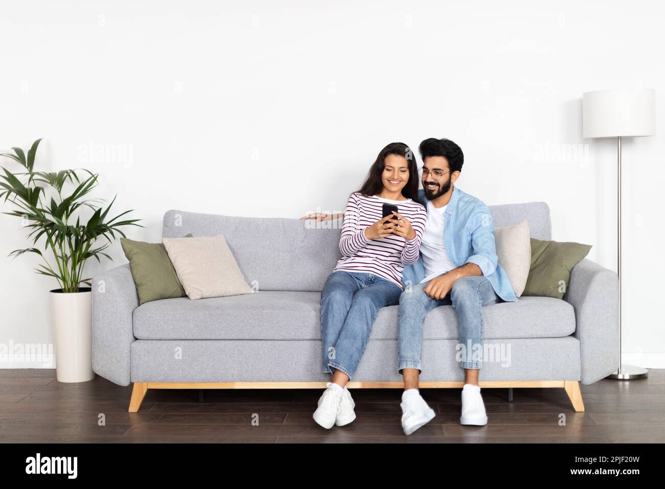Relaxed multicultural couple sitting on sofa, using smartphone Stock Photo