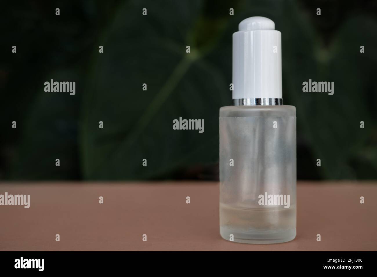 A transparent vial with no label and a plastic white cover containing colorless liquid on a background with plants. Empty space for text Stock Photo