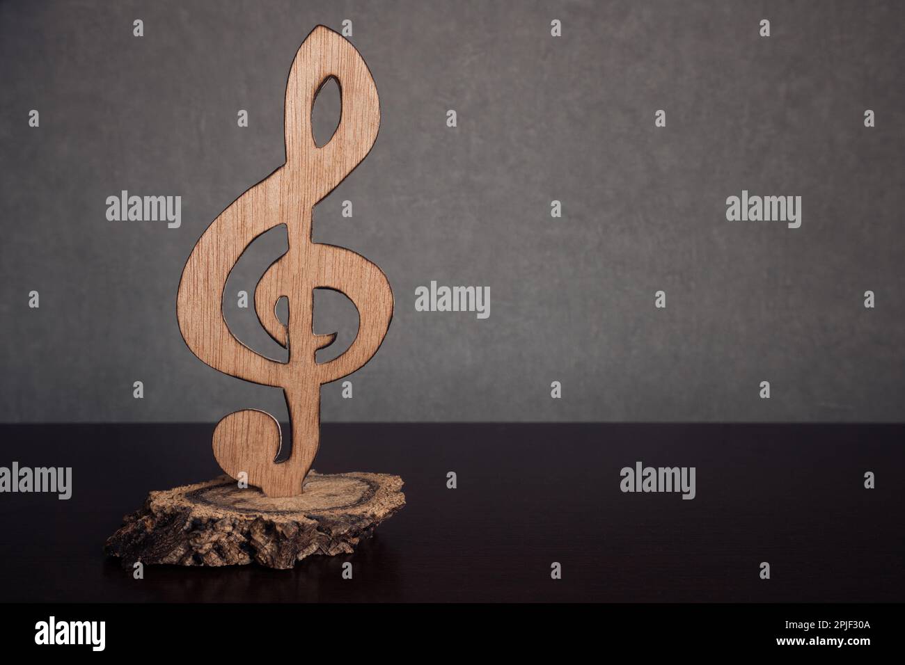 A treble clef statuette carved in wood isolated against a dark background with empty space for text. Symbol of music Stock Photo