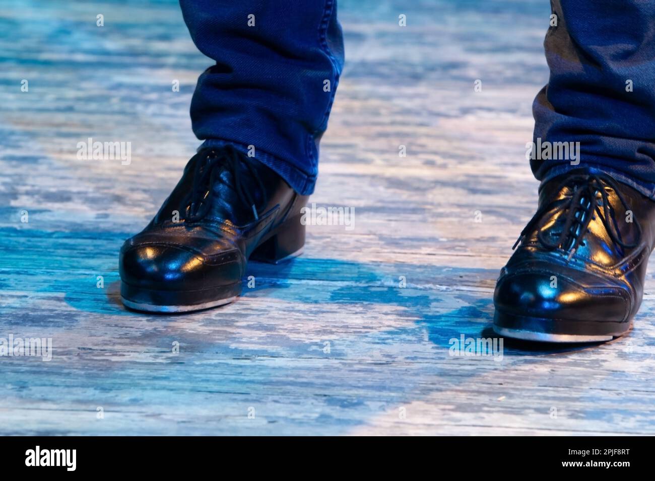 Men's legs in motion in stage trousers with stripes and leather shoes for Irish dancing on the floor. Black work boots for tap dancing with reflection Stock Photo