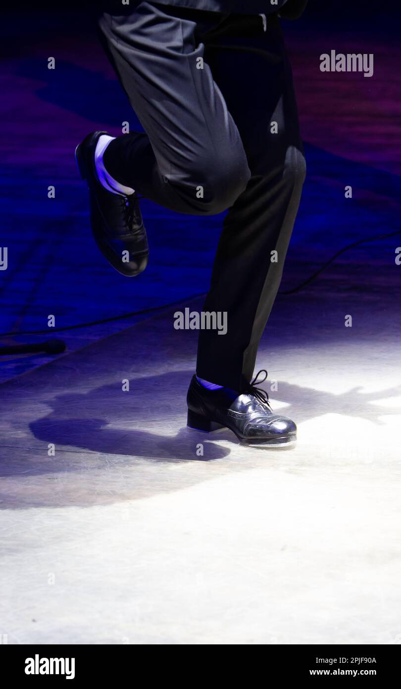 Men's legs in motion in stage trousers with stripes and leather shoes for Irish dancing on the floor. Black work boots for tap dancing with reflection Stock Photo