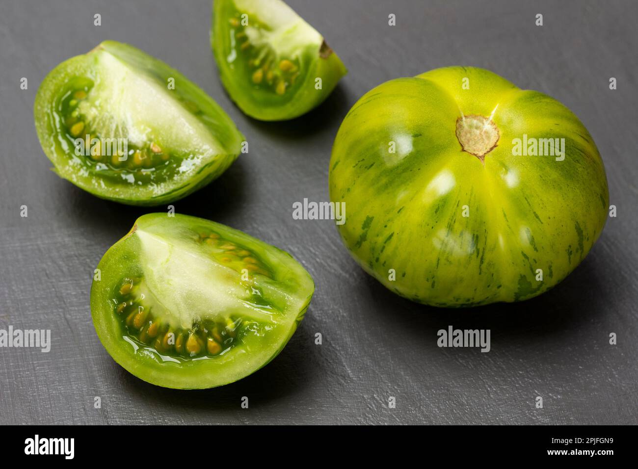 Halves of a green tomato, a whole tomato on a gray background. Top view. Stock Photo