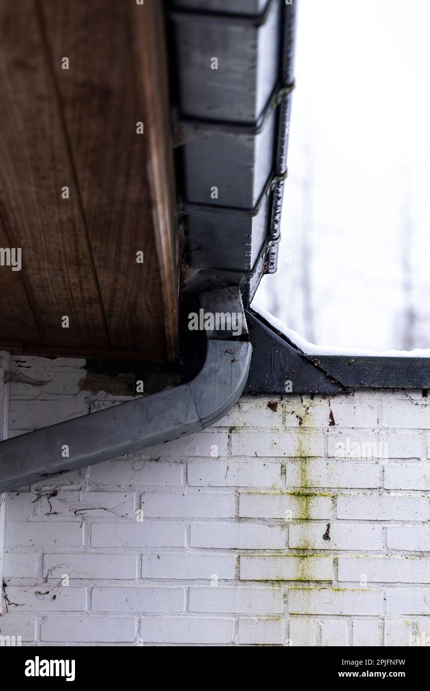 A portrait of a broken metal drain pipe connected to the gutter of a