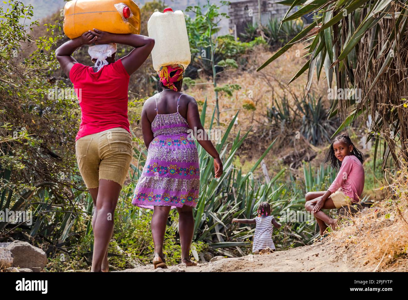 Two women and a child carrying water canisters as heavy load on their heads, Santiago Island, Cape Verde Islands Stock Photo
